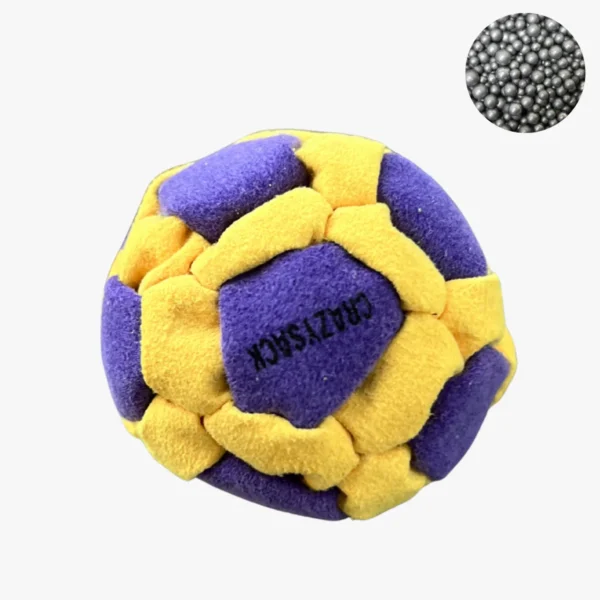 Ein gelb lila Footbag mit blauen Akzenten liegt auf einem hellgrauen Untergrund