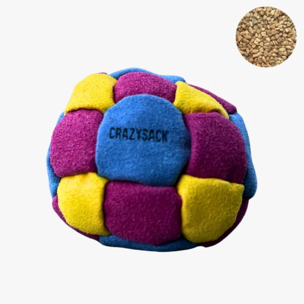 Ein gelb lila pink gemusterter Footbag liegt auf einem grauen steinigen Boden