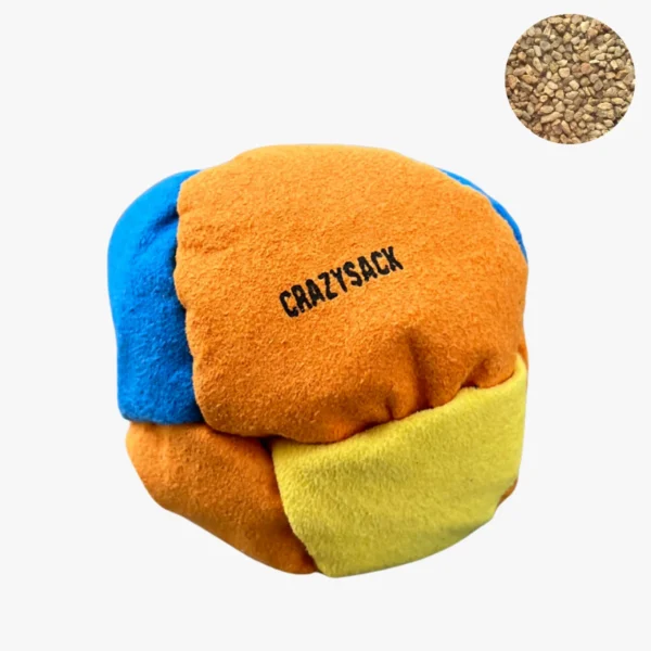 Ein gelb orange blauer Footbag liegt draußen auf einem Kiesboden