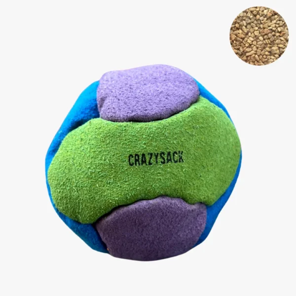 Ein grün lila hellblauer Footbag liegt auf einem grauen Kiesuntergrund