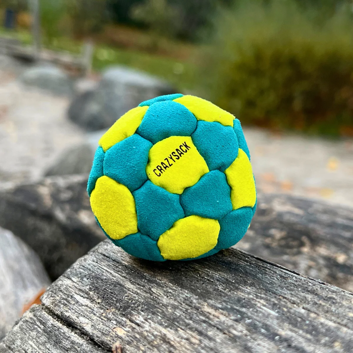 Ein hellblau gelber Footbag liegt auf einem Felsen mit Parkhintergrund