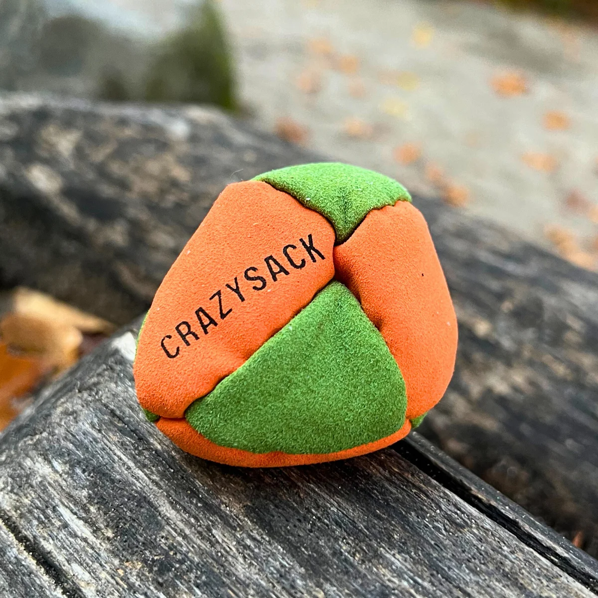 Ein orange grün Footbag liegt auf einem Holzstamm im Herbstlaub