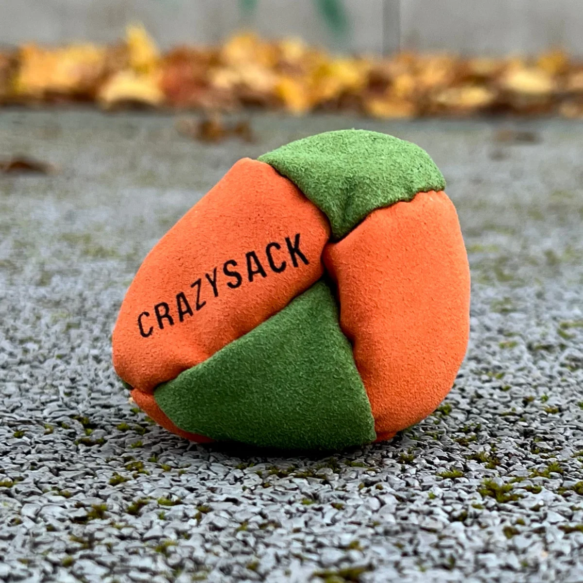Ein orange grün Footbag liegt draußen auf grauem Kies