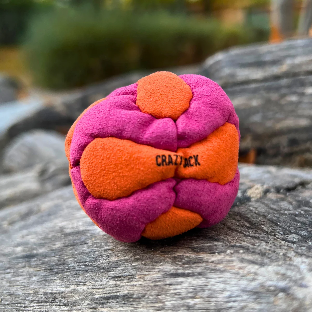 Ein orange pink Footbag liegt im Freien auf grauem Untergrund