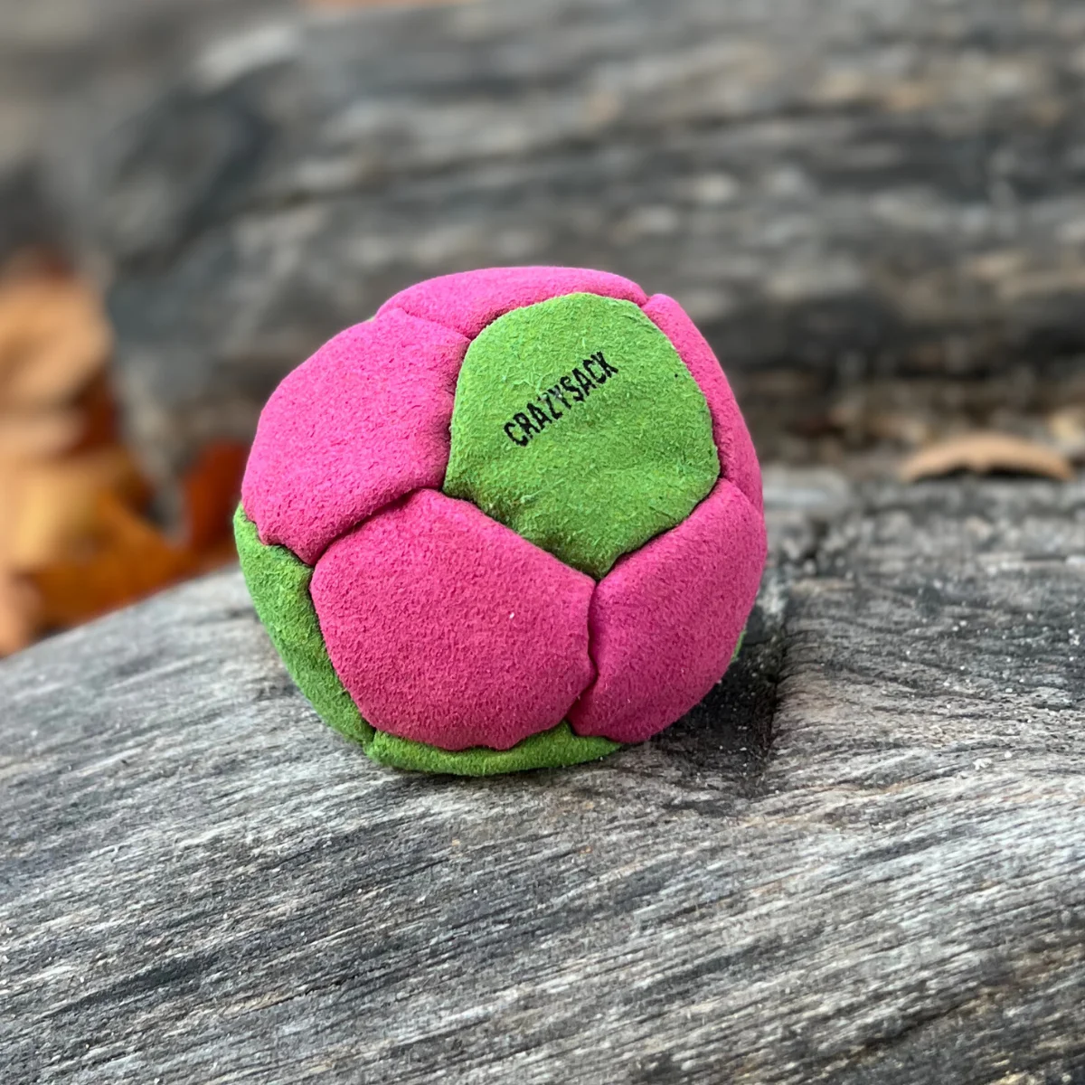 Ein pink grüner Footbag liegt draußen auf einem Holzstamm