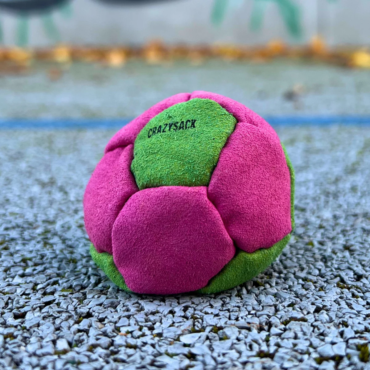 Ein pink grüner Footbag steht auf einem grauen Untergrund im Außenbereich